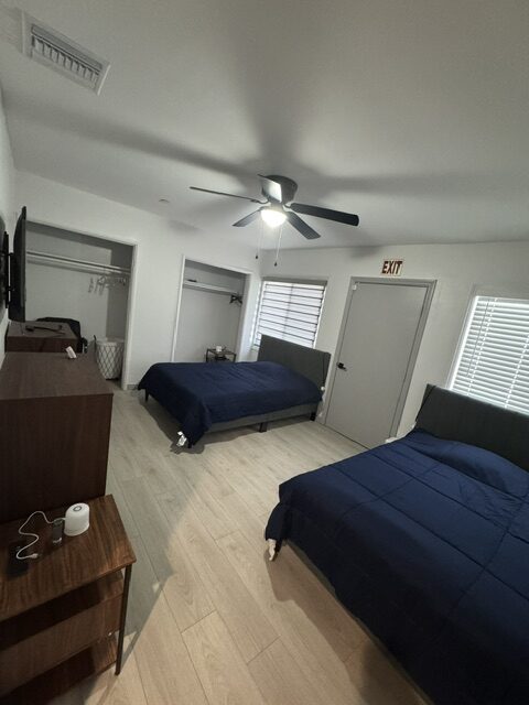 Resident bedroom with two beds, wood dressers, and a ceiling fan