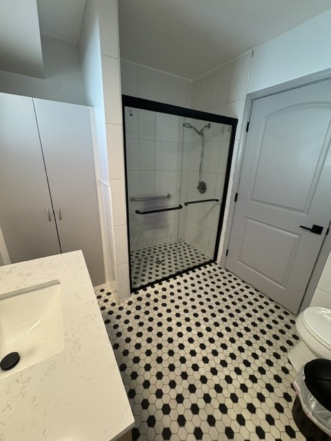 Private bathroom with a walk-in shower, grab bar, and black-and-white tile floor